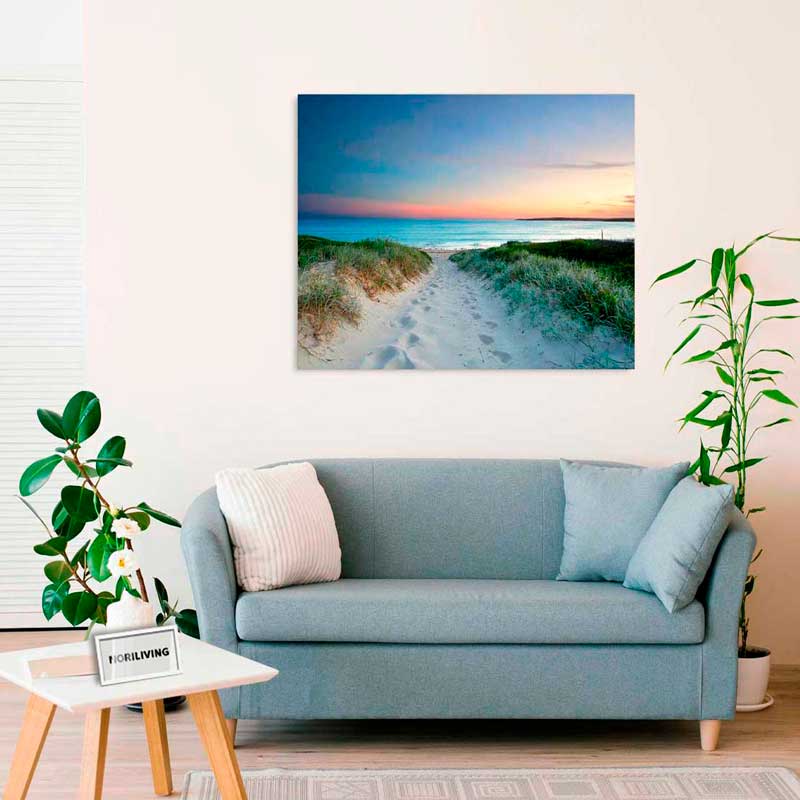 Modernes Wohnzimmer mit blauer Couch, grünen Pflanzen und einem Leinwandbild, das einen Strandweg bei Sonnenuntergang zeigt.