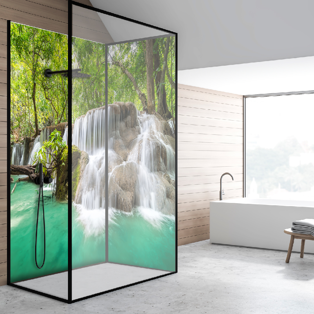 Eine stilvolle Duschkabine mit einem Design, das einen natürlichen Wasserfall inmitten eines Waldes zeigt, daneben eine freistehende Badewanne vor einem großen Fenster.