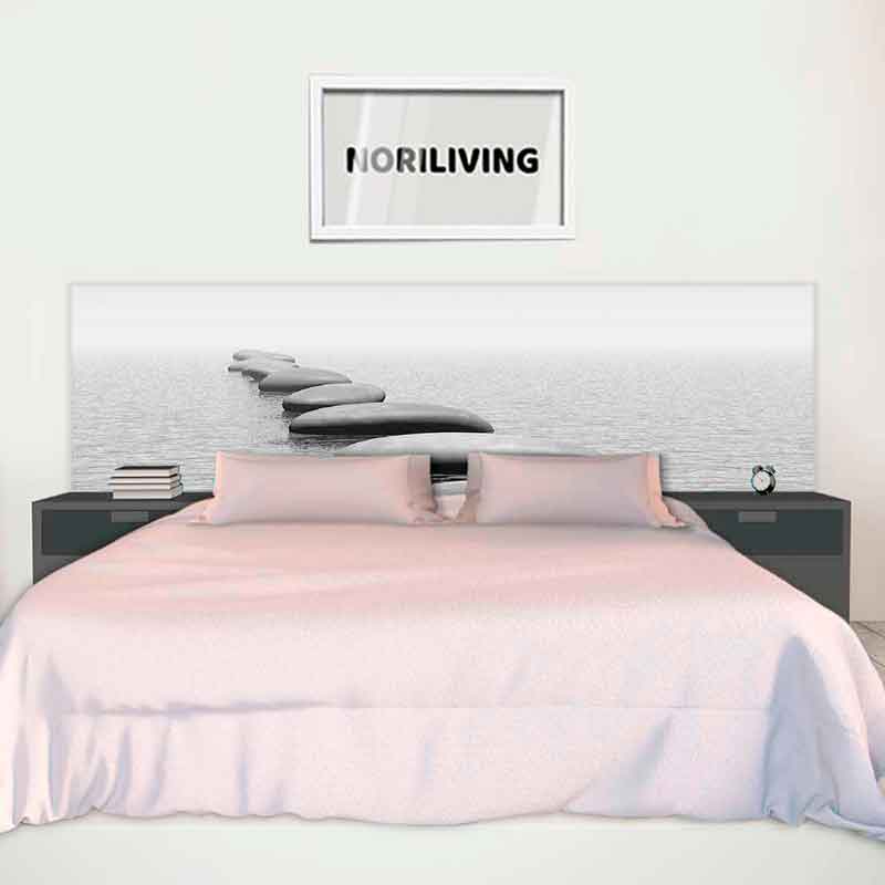 Ein großes Bett mit rosa Bettwäsche steht vor einer Wand mit einem Zen-Stein-Motiv. Links und rechts sind Nachttische mit Büchern und einer Uhr. An der Wand hängt ein Bild mit der Aufschrift 'NORILIVING'.