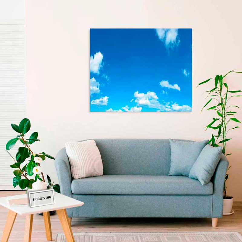 Ein stilvolles Wohnzimmer mit einem blauen Sofa, Pflanzen und einer Leinwand, die einen blauen Himmel mit weißen Wolken zeigt.