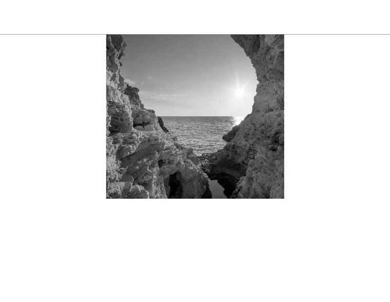 Schwarzweißfoto von einer Felsformation am Meer bei Sonnenuntergang