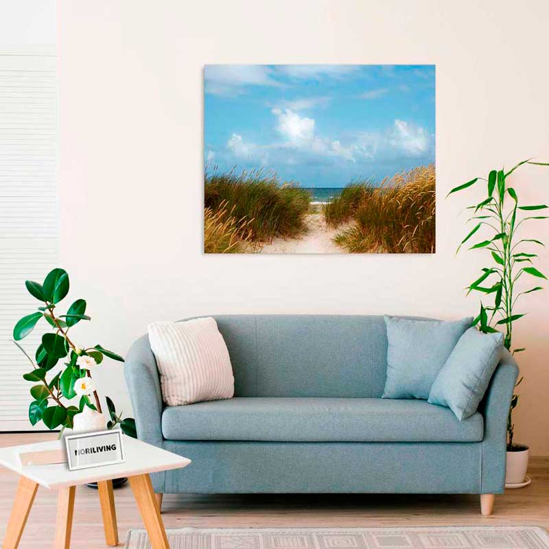 Gemütliches Wohnzimmer mit blauer Couch, Pflanzen und Leinwandbild eines Strandwegs